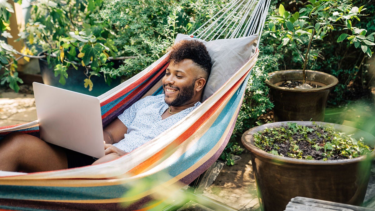 Man relaxing in hammock working on laptop computer