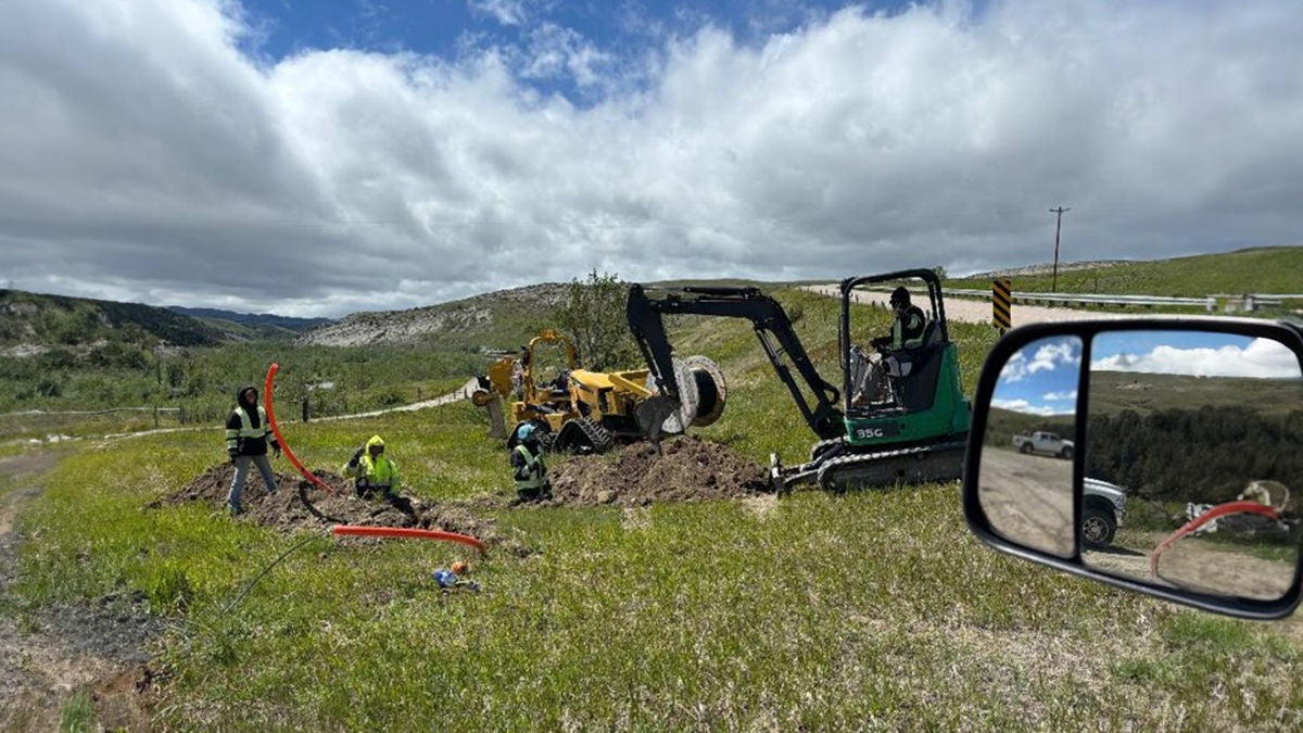 A tribal rural mountain range with a tractor and workers installing wires in the ground