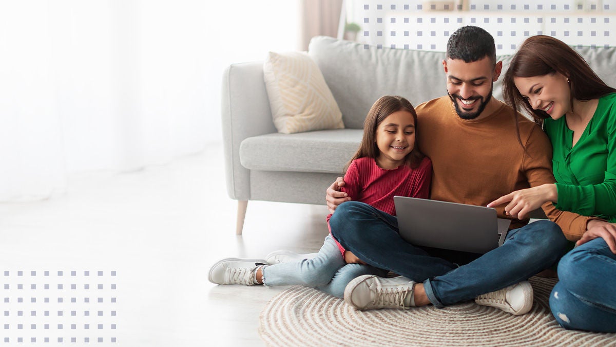 A smiling family sitting together on the floor while viewing a laptop