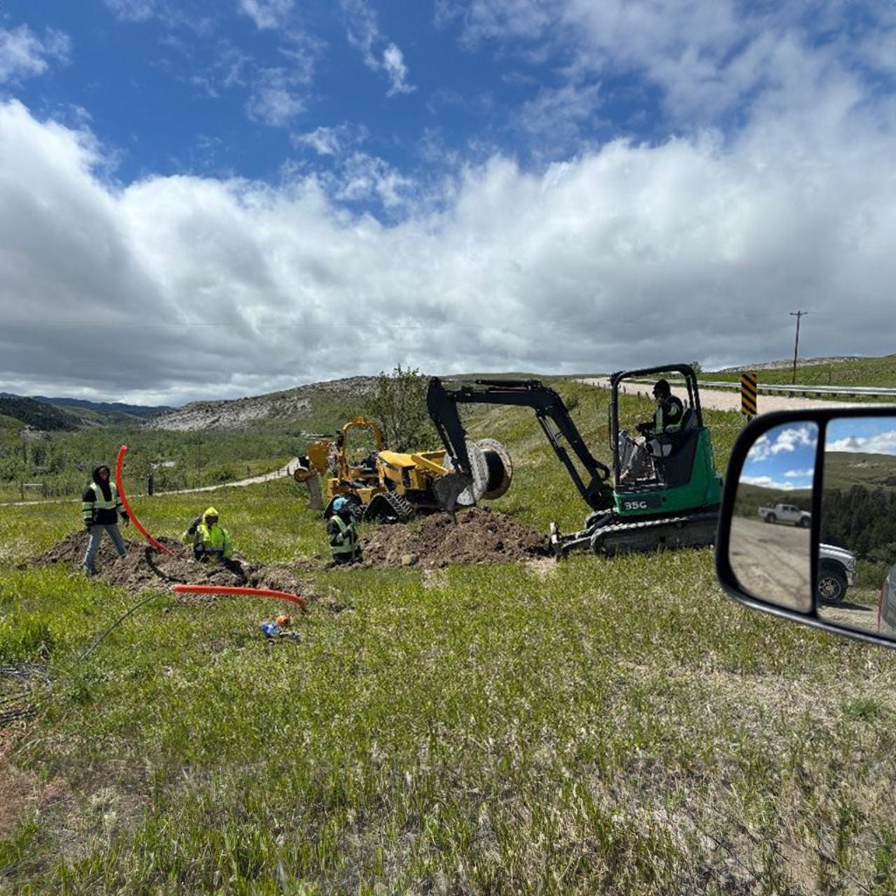 A tribal rural mountain range with a tractor and workers installing wires in the ground