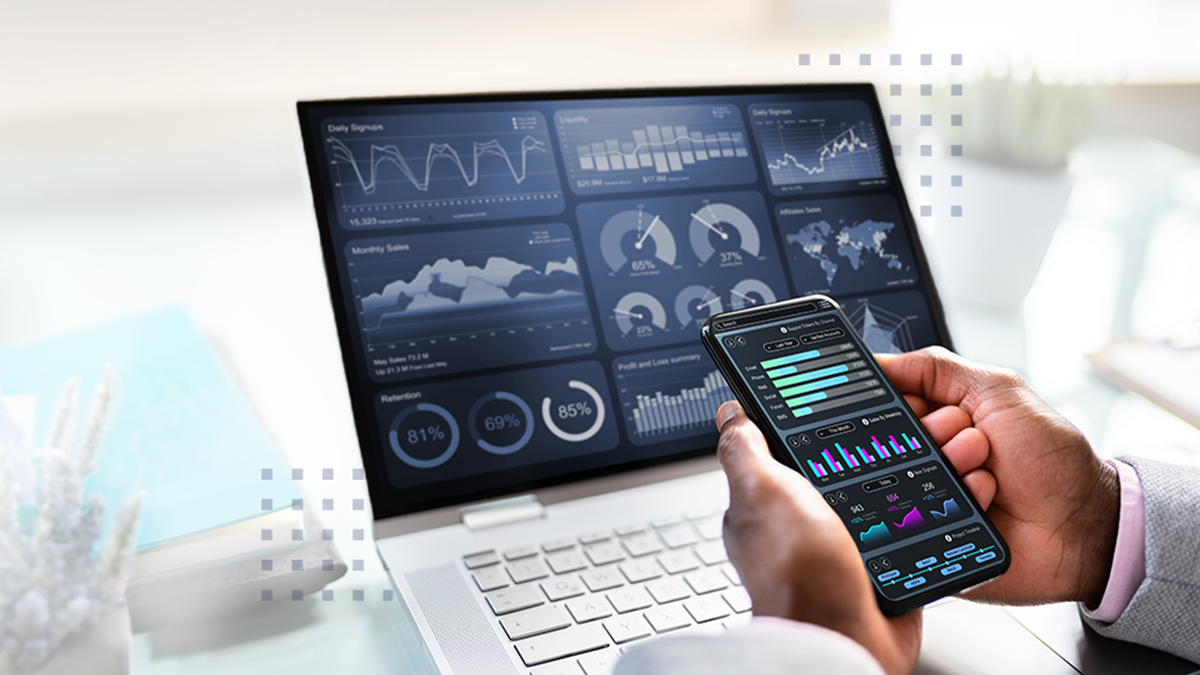 A man holding a cell phone in front of a laptop showing business data charts